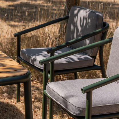 Campus outdoor Dining chair in bottle green powder coat with grey cushions and a matching teak slatted table on a dry grass lawn.