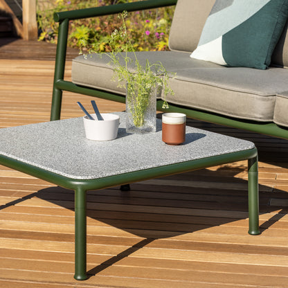 Detail of a Campus Coffee table in bottle green and light granite top with a clear Causeway vase and bowl on top. detail shows the tubular frame and the flared signature foot of the campus range. 