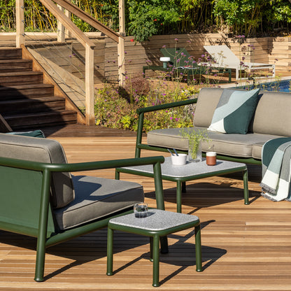 Detail of the Campus 3 seat sofa and 2 seat sofa with a coffee table and side table in bottle green and light granite on a modern teak desk in front of a swimming pool with Eos platform loungers in the background