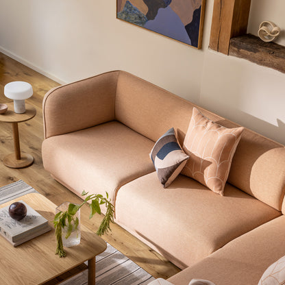Meris sectional sofa in blush coloured fabric in a warm, styled living room setting with wooden floors, a port coffee and side table in Oak, and scales and eclipse pillows.