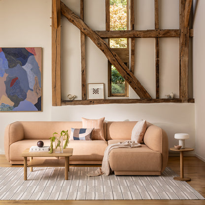 Meris Sectional Sofa by Monica Armani in a blush pink fabric styled with scales and eclipse cushions and throws with the Port side and coffee table in a modern barn conversion house with exposed timber joists and modern artwork on the wall