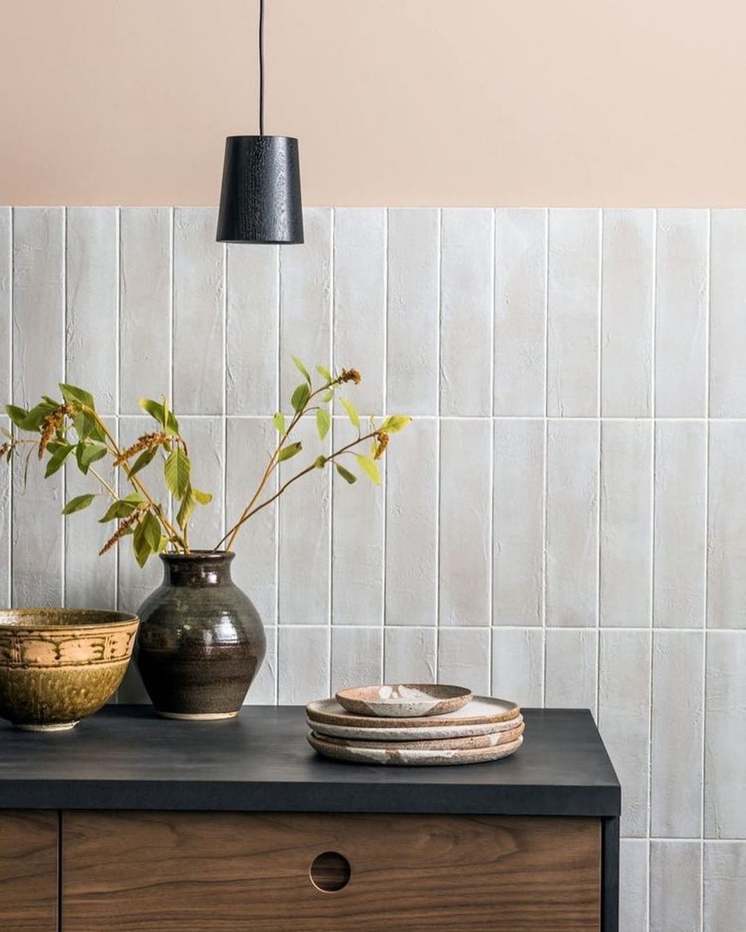 Black pendant light on top of ceramic vases, and stacked plates.