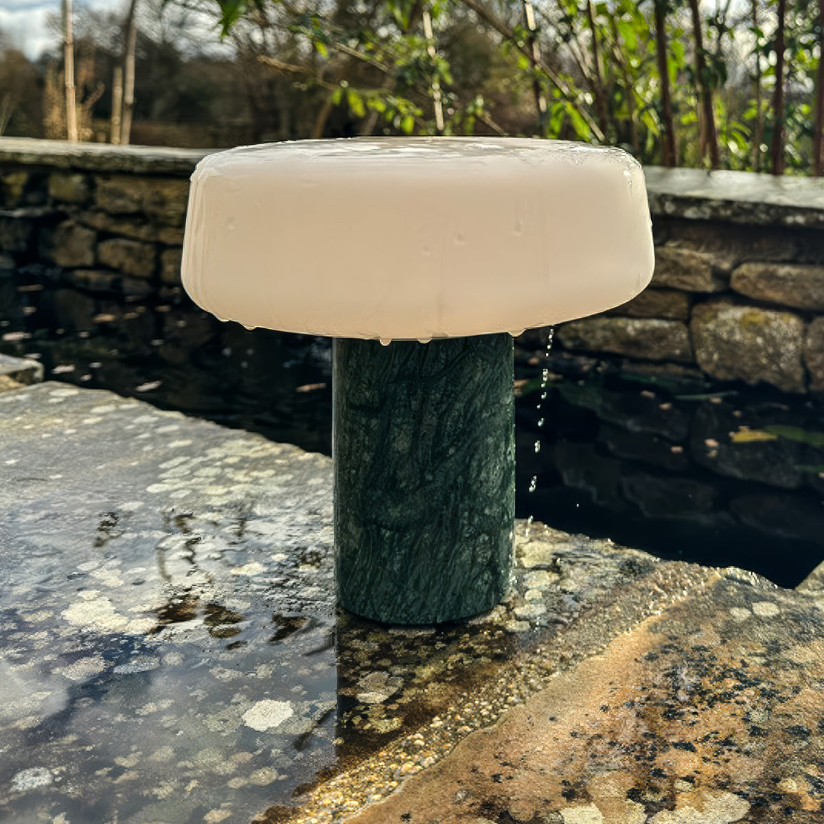 Solid rechargeable table light in Guatemala marble with opalised glass sat on a wall after a rain storm showing its waterproof design and outdoor use. 