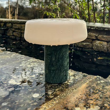 Solid rechargeable table light in Guatemala marble with opalised glass sat on a wall after a rain storm showing its waterproof design and outdoor use. 