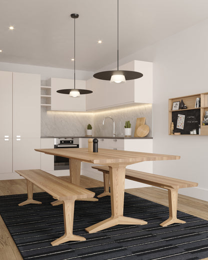 A modern dining area featuring a light oak wood table with matching bench seats, set on a dark striped area rug. The space is lightened by the sculptural Sum Pendant.